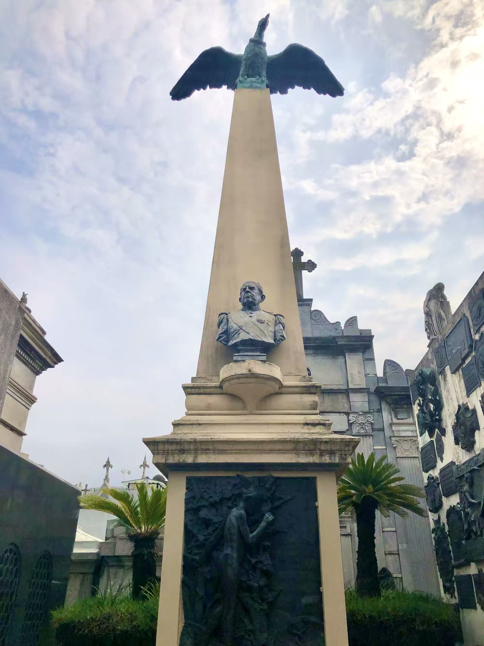 照片中是曾于1868年至1874年担任阿根廷第七任总统的多明戈·福斯蒂诺·萨米恩托（Domingo Faustino Sarmiento）的墓地。这座标志性的纪念碑的墓碑呈方尖碑造型，顶部雕刻着一只展翅的神鹫，下方镶嵌着萨米恩托的半身铜像以及精美的青铜浮雕，右侧的墙壁上挂满了后人致敬的纪念牌匾。萨米恩托前总统大力推动了阿根廷的基础教育和现代化建设，在阿根廷被广泛尊称为“教育之父”。